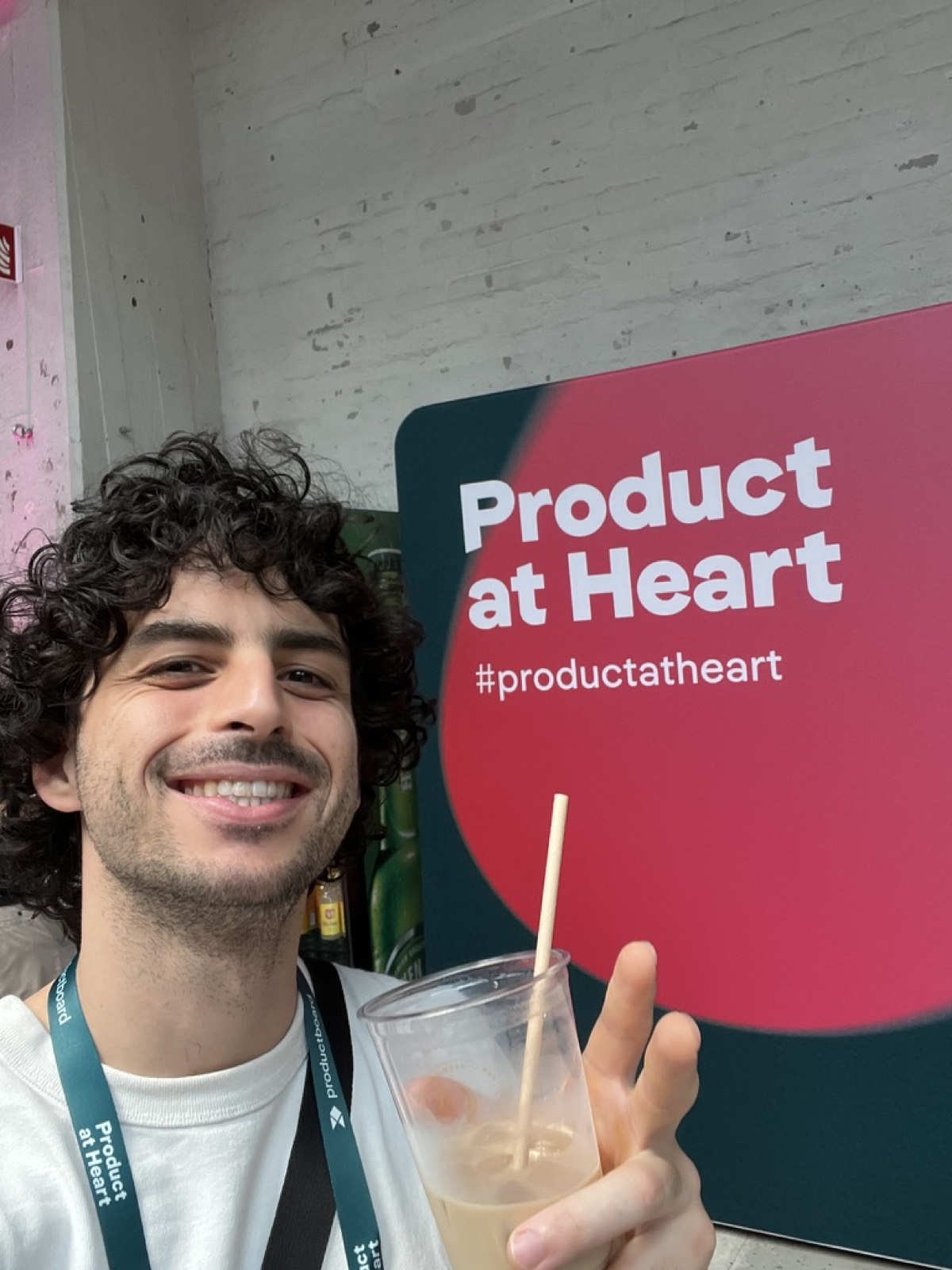 Selfie no evento, com o painel do Product at Heart ao fundo